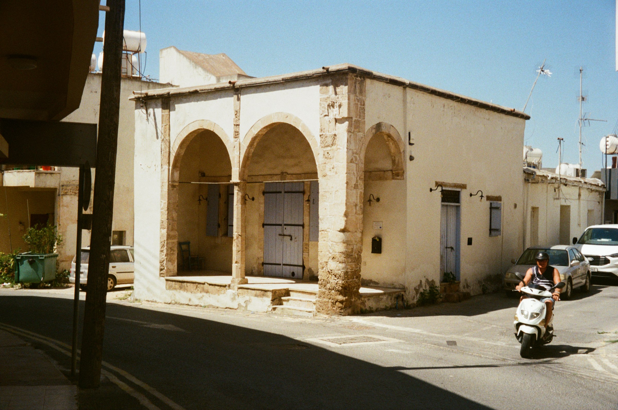 A stone archway building on a street corner, moped passing by